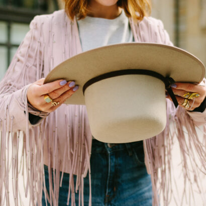 Frau in Fransenjacke hält beigen Filzhut