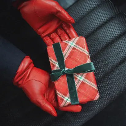 Geschenke Guide Rote Handschuhe aus Leder mit Geschenk in rot kariertem Papier mit grünen Akzenten auf einem Autositz
