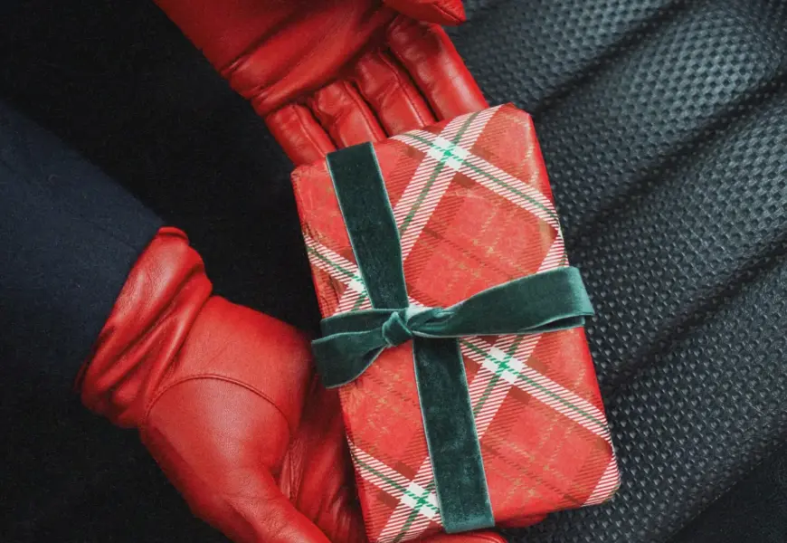 Geschenke Guide Rote Handschuhe aus Leder mit Geschenk in rot kariertem Papier mit grünen Akzenten auf einem Autositz